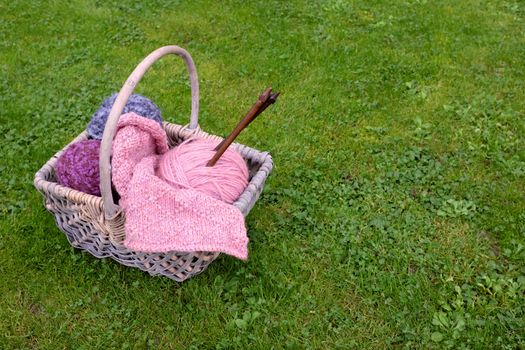 Woven basket of knitting, wooden needles and soft yarn on green grass