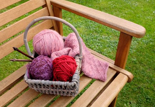 Craft basket of patterned knitting, balls of wool and wooden needles on a garden bench