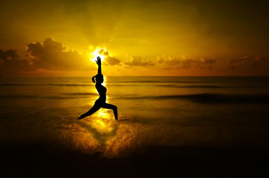 Silhouette of female doing yoga meditation during sunrise with natural golden sunlight at beach.