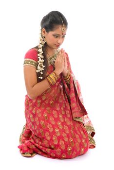 Indian girl in a greeting pose, traditional sari costume, full length kneeling on floor isolated on white background