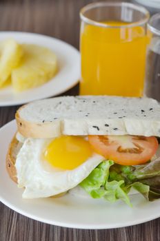 sandwich with tomatoes , lettuce and fried egg on dish , served with juice and fruits 