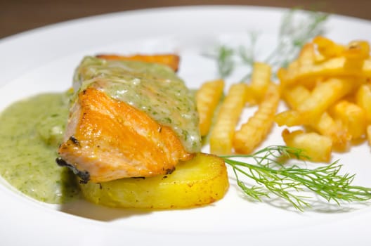 close up salmon steak served with green sauce and french fries  on white plate