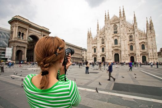 Young woman taking picture of Duomo di Milano (Milan Cathedral), Milan, Italy, motion blurred people on square