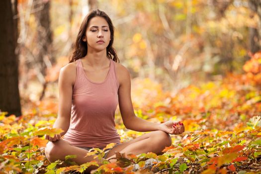 Beautiful young girl meditating in autumn park