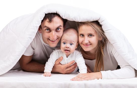 Young family with baby boy under blanket on bed at home