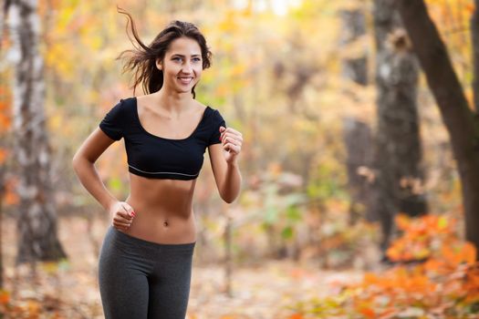 Happy young woman running in autumn forest