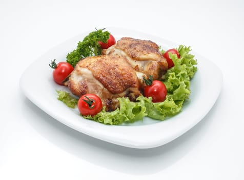 Fried chicken pieces on a plate with tomatoes, lettuce and parsley. Taken on a sheet of white plastic. Is not an isolate.