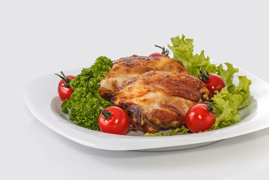 Fried chicken pieces on a plate with tomatoes, lettuce and parsley. Taken on a sheet of white plastic. Is not an isolate.