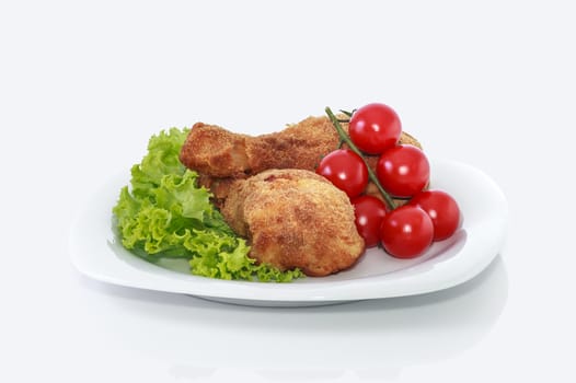 Fried chicken pieces on a plate with lettuce and tomatoes. Taken on a sheet of white plastic. Is not an isolate.