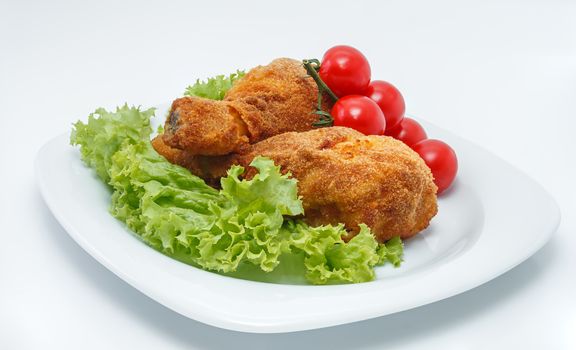 Fried chicken pieces on a plate with lettuce and tomatoes. Taken on a sheet of white plastic. Is not an isolate.