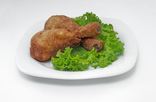 Fried chicken pieces on a plate with lettuce. Taken on a sheet of white plastic. Is not an isolate.