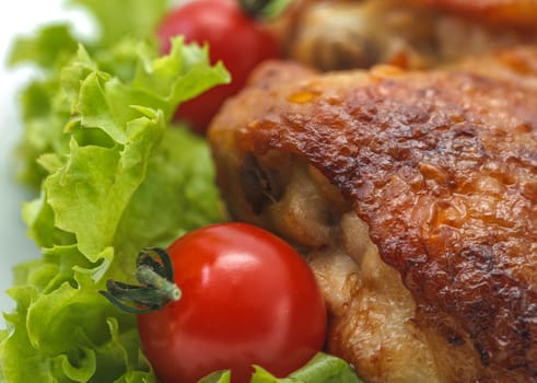 Fried chicken pieces on a plate with lettuce and tomatoes. Taken on a sheet of white plastic. Is not an isolate.