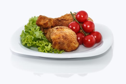 Fried chicken pieces on a plate with lettuce and tomatoes. Taken on a sheet of white plastic. Is not an isolate.