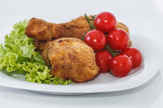 Fried chicken pieces on a plate with lettuce and tomatoes. Taken on a sheet of white plastic. Is not an isolate.