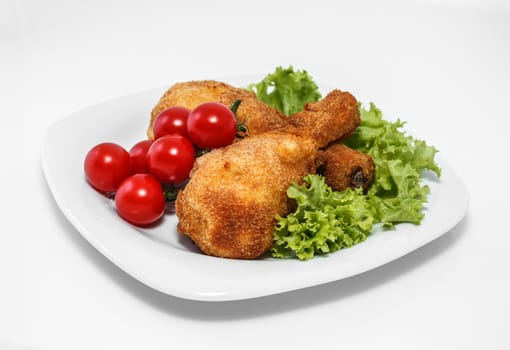 Fried chicken pieces on a plate with lettuce and tomatoes. Taken on a sheet of white plastic. Is not an isolate.