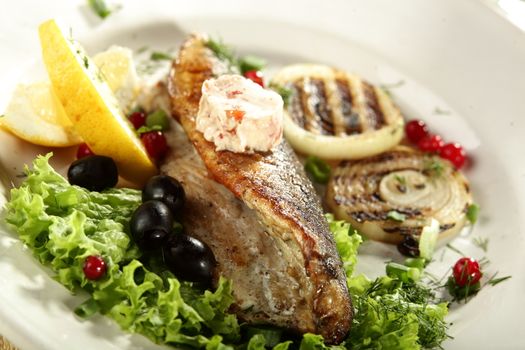 hot fish in white dish with olives and lemon