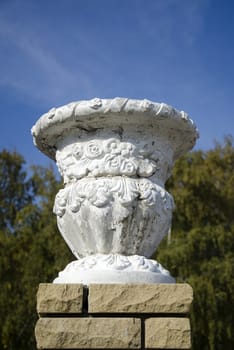 The Old plaster garden vase on a modern brick pedestal on tree background