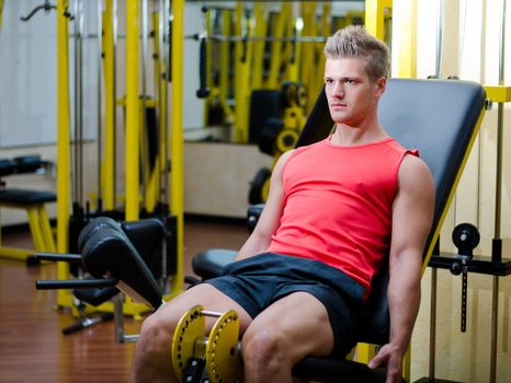 Attractive and fit young man in gym working out legs and exercising on equipment