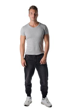 Attractive young muscle man in grey t-shirt and sporty pants, isolated on white background