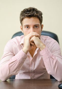 Serious, attractive young office worker in shirt at his desk, looking at camera