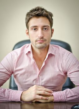 Serious, attractive young office worker in shirt at his desk, looking at camera