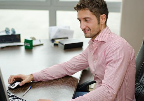 Attractive young businessman sitting at desk in his office working with computer