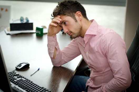 Preoccupied, worried young male worker staring at computer screen in his office