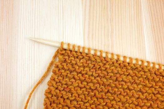 Garter stitch in deep orange yarn on a knitting needle, on pine board