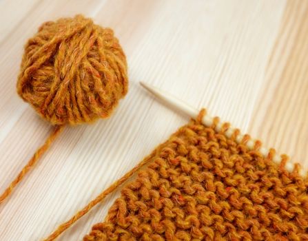 Closeup of garter stitch knitting on the needle with a ball of orange wool