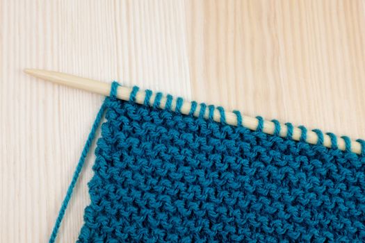 Length of garter stitch in blue yarn on knitting needle, on wooden background