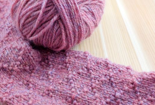 Patterned knitting in pink yarn with ball of wool, on wooden table