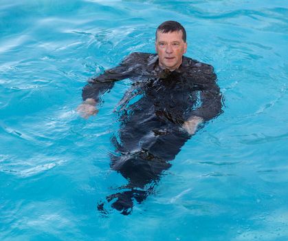 Senior caucasian businessman in suit up to waist in deep blue water and looking worried as he tries to keep afloat