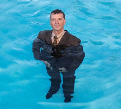 Senior caucasian businessman in suit up to waist in deep blue water and smiling at the camera