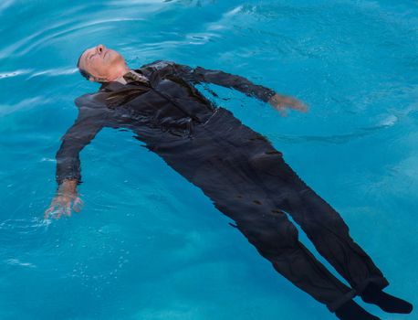 Senior caucasian businessman in suit sinking underwater in deep blue pool looking like drowning as a result of problems