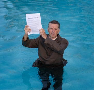 Senior caucasian businessman in suit up to waist in deep blue water worried about being underwater with mortgage payments