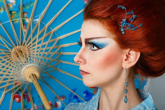 Attractive geisha in a smart dress with an umbrella, photographed in the studio