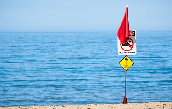 A jellyfish or marine stinger warning sign and red flag at a tropical Australian beach.