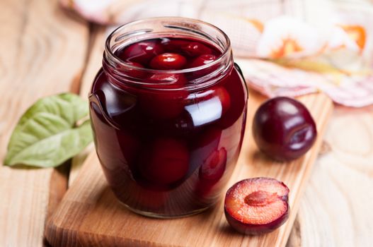 Homemade plum jam in glass jar on wooden table.