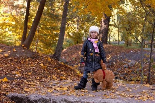 Adorable girl with teddy bear outdoors on beautiful autumn day