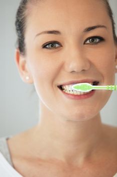 Pretty young woman smiling and cleaning her teeth with a toothbrush, head and shoulders portrait