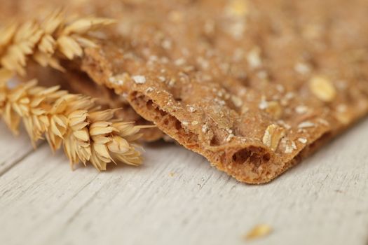 Ear of ripe golden wheat with a wheat cracker or crispbread on a white wooden surface with shallow dof