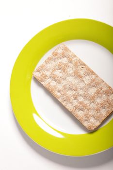 Overhead view of a single wheat cracker on a plate with a green border over a white background