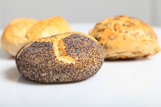 Low angle view of a single freshly baked crusty poppy seed roll with two additional assorted rolls visible behind, shallow dof