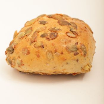 Crusty golden roll with roasted sunflower seeds, close up view over white