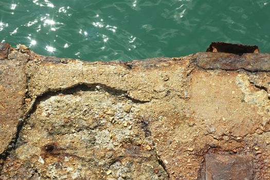 Detail of old reinforced concrete pier over the water in a bright sunlight