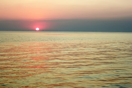 Red sun in the clouds near the horizon over the sea bay