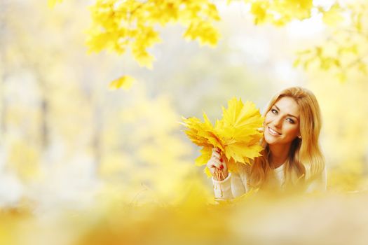 Young woman laying down on the ground covered dry autumnal foliage in beautiful park