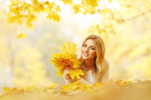 Young woman laying down on the ground covered dry autumnal foliage in beautiful park