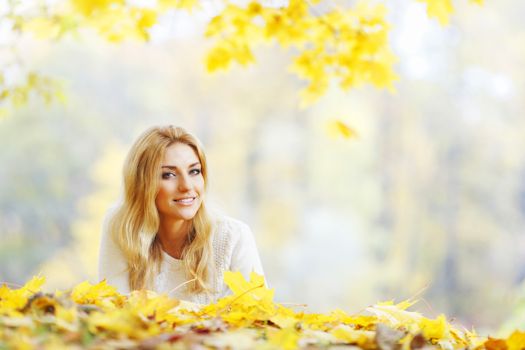 Young woman laying down on the ground covered dry autumnal foliage in beautiful park