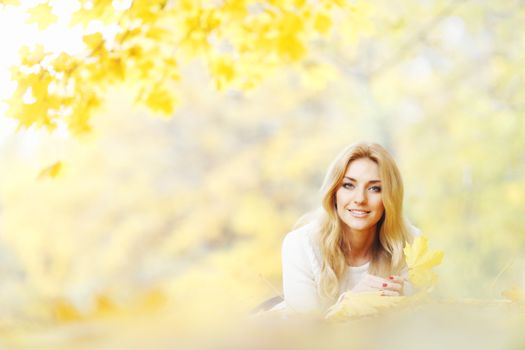 Young woman laying down on the ground covered dry autumnal foliage in beautiful park